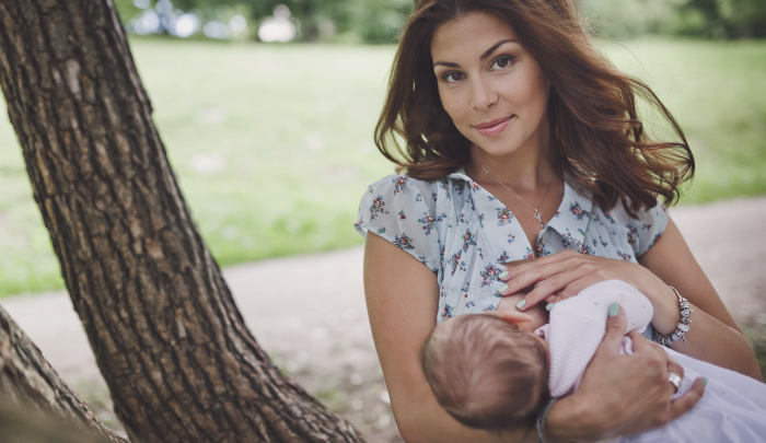 mother smiling as she breastfeeds her nursing baby under a tree
