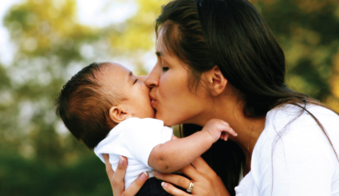 Mother holding and kissing infant child in her arms