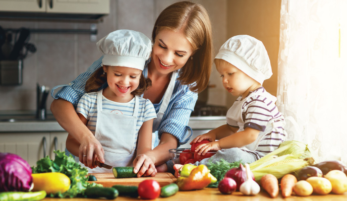 Mother with two young children helping to prepare a meal in the kitchen All three smiling