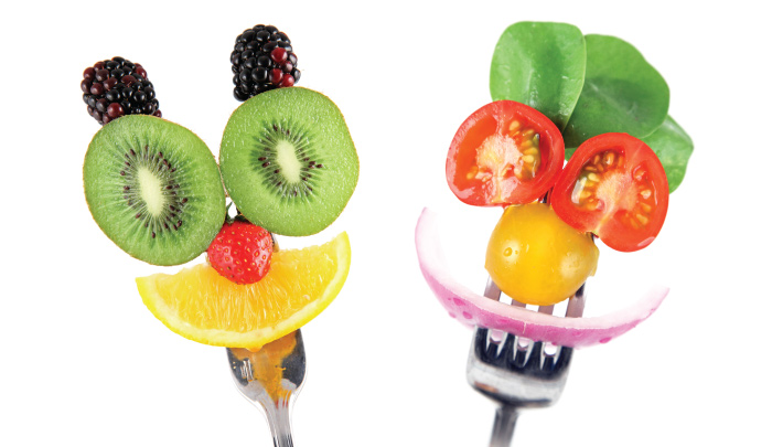 funny faces made from slices of various fruits and vegetables on held together on a pair of forks